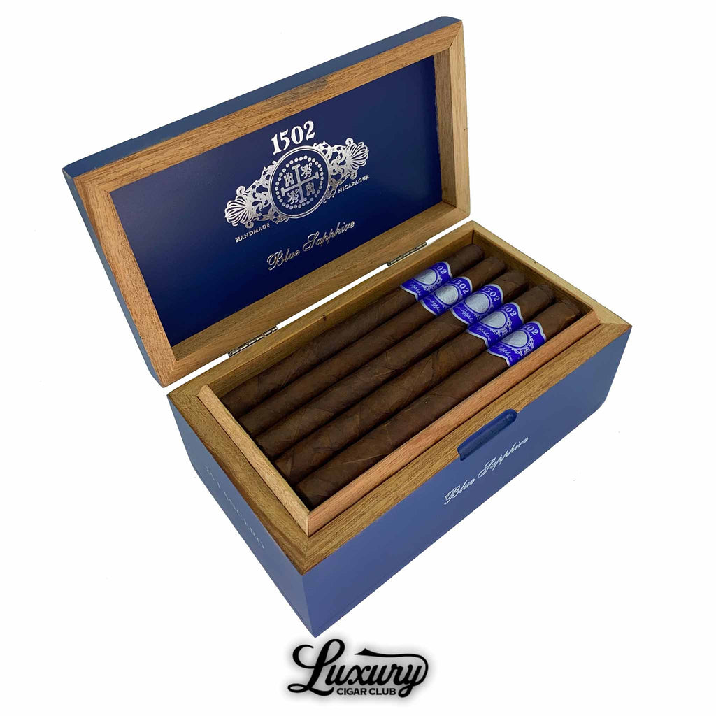 Open box of 1502 Blue Sapphire cigars with blue and silver bands, neatly arranged in a premium cedar-lined box, showcased by Luxury Cigar Club.