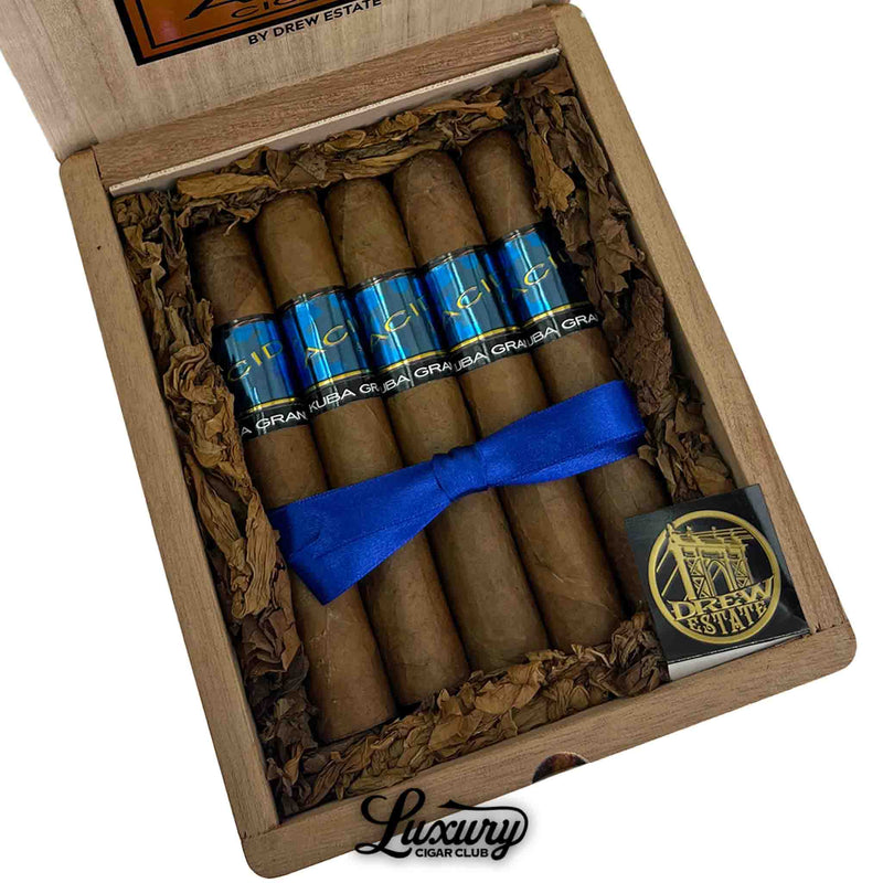 Detailed close-up view of ACID Kuba Kuba Grande cigars in a wooden box, showing blue cigar bands, decorative ribbon, and the Luxury Cigar Club logo.