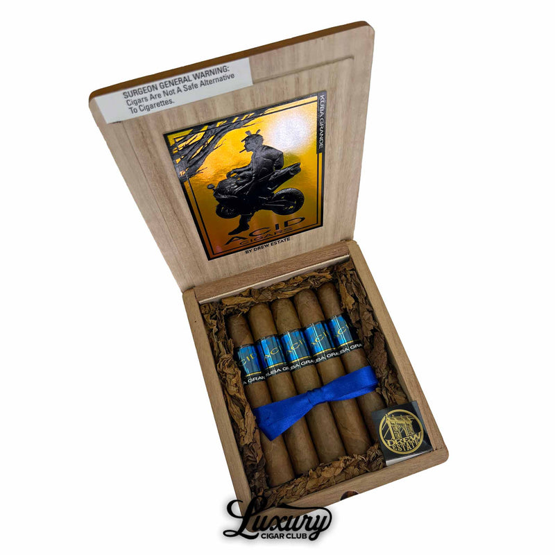 Open wooden cigar box containing ACID Kuba Kuba Grande cigars by Drew Estate, featuring blue and black bands, arranged neatly with a blue ribbon, displayed with the Luxury Cigar Club logo.