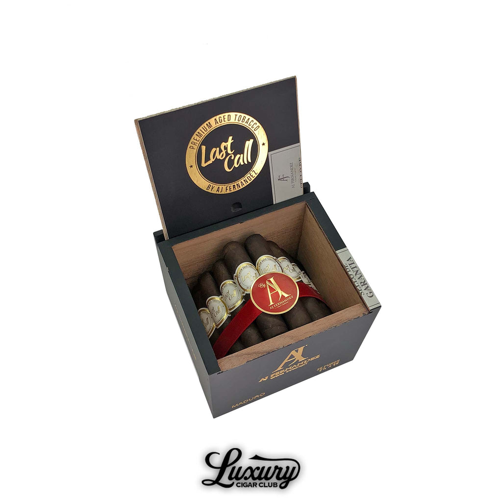 Luxury Cigar Club product photo of AJ Fernandez Last Call Maduro Chiquitas cigars displayed in an open black and gold box, showing short dark brown chiquita cigars bundled with a red ribbon and AJ Fernandez medallion band.