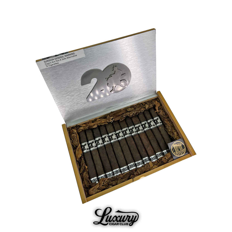 Open box of Acid 20 Maduro Robusto cigars featuring dark wrappers, silver and black bands, decorative tobacco leaf lining, and a commemorative coin, with "20" logo on metallic lid and Luxury Cigar Club branding below.
