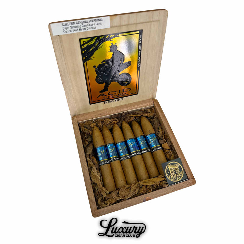 Open box of Acid Blondie Belicoso cigars by Drew Estate, featuring cigars with light Connecticut wrappers and vibrant blue bands, nestled in shredded tobacco. The inside lid displays the iconic Acid Cigars silhouette artwork. Luxury Cigar Club logo appears below.