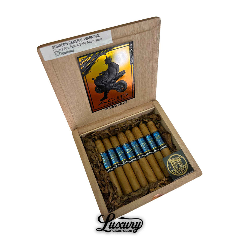 Open box of Acid Blondie cigars by Drew Estate, featuring short cigars with light Connecticut wrappers and bright blue bands, resting in shredded tobacco. The inside lid displays the iconic Acid silhouette artwork. Luxury Cigar Club logo is shown at the bottom.
