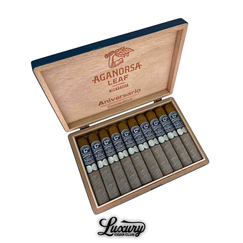 Open wooden box of Aganorsa Leaf Aniversario Connecticut Gran Robusto cigars, featuring ten cigars with golden Connecticut wrappers, dark blue and silver bands, and gray foot sleeves. The inside lid is engraved with the Aganorsa Leaf logo and “Aniversario Connecticut.” The Luxury Cigar Club logo is shown below the box.