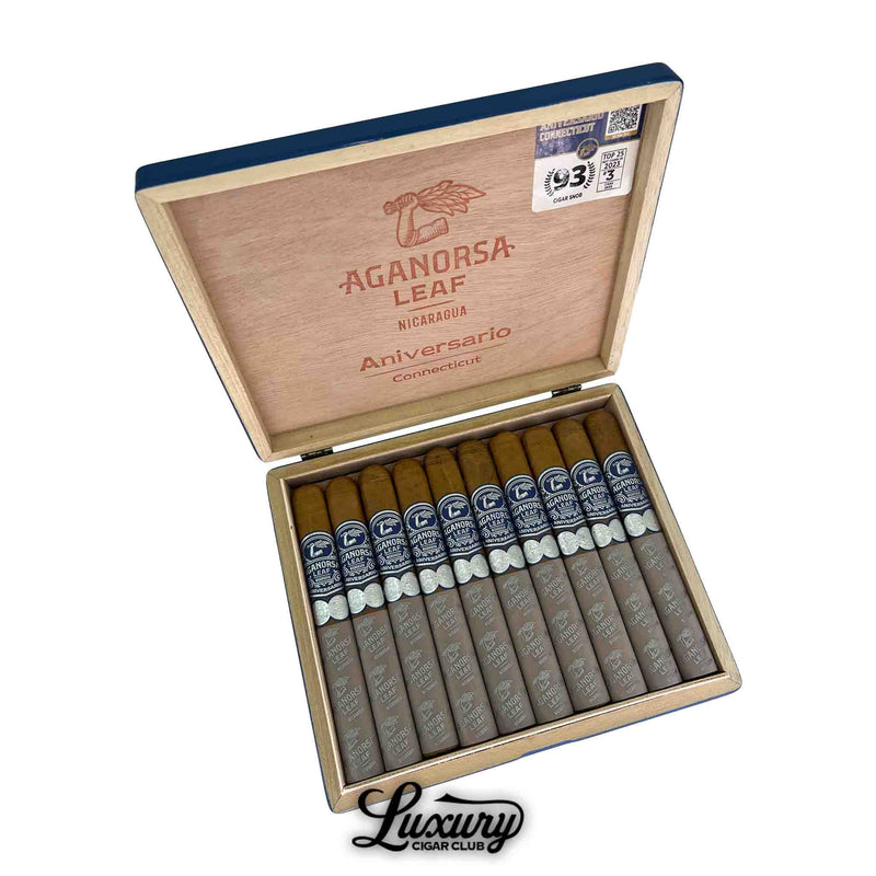Open wooden box of Aganorsa Leaf Aniversario Connecticut Toro cigars, featuring ten light brown cigars with dark blue bands and gray foot sleeves. The inside lid displays the Aganorsa Leaf logo, “Aniversario Connecticut,” and a “93 Rated” sticker. The Luxury Cigar Club logo appears below the box.