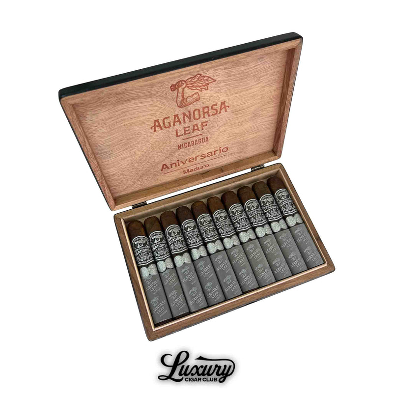 Open box of Aganorsa Leaf Aniversario Maduro Gran Robusto cigars, featuring dark, rich wrappers with black and silver bands, neatly arranged in a wooden box engraved with the brand's logo and "Aniversario Maduro" on the lid.