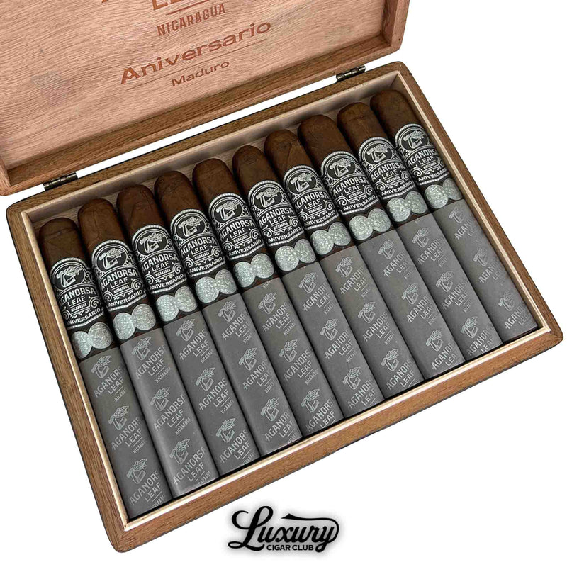 Close-up of Aganorsa Leaf Aniversario Maduro Gran Toro cigars neatly arranged in a wooden box, featuring dark brown wrappers, black and silver bands, and silver foot sleeves with Aganorsa Leaf branding.