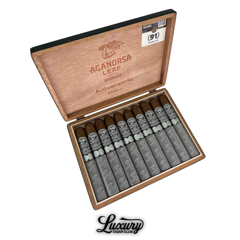 Open box of Aganorsa Leaf Aniversario Maduro Gran Toro cigars featuring ten cigars with dark maduro wrappers, silver and black bands, and silver foot sleeves. The inside lid is branded with the Aganorsa Leaf logo and “Aniversario Maduro.”