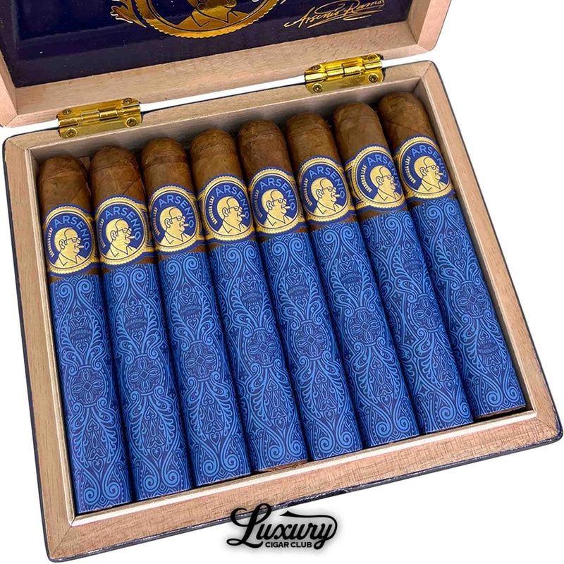 Close-up of Aganorsa Leaf Arsenio Robusto cigars inside an open humidor-style box, highlighting the ornate blue and gold wrapping and precise cigar arrangement. The presentation reflects classic Nicaraguan artistry. Luxury Cigar Club.