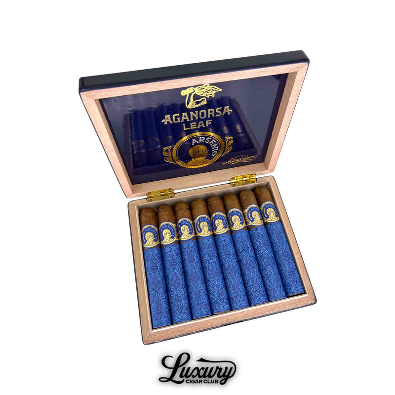 Open wooden box of Aganorsa Leaf Arsenio Robusto cigars showing eight beautifully wrapped cigars in blue and gold. The inside lid features the Aganorsa Leaf and Arsenio branding in gold on a deep blue background, emphasizing premium craftsmanship. Luxury Cigar Club.