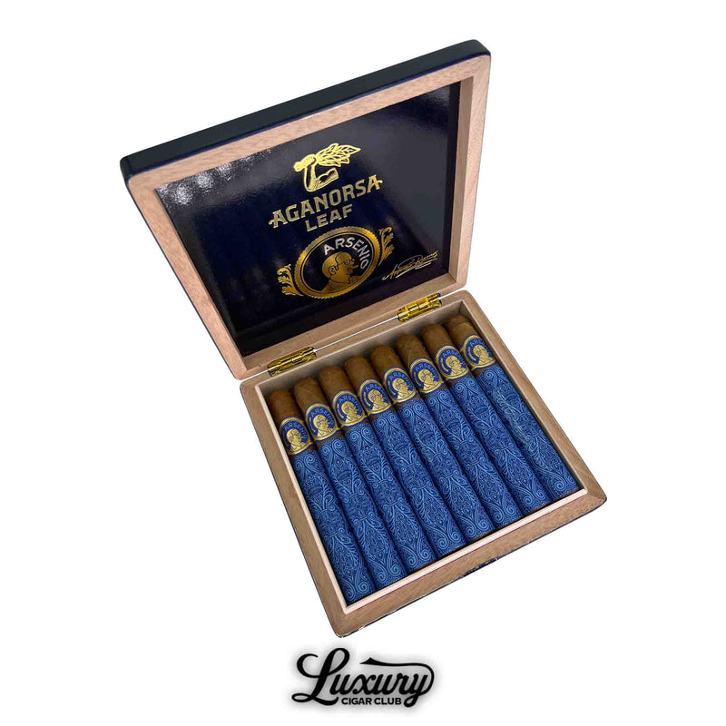 Open box of Aganorsa Leaf Arsenio Toro cigars, featuring blue and gold decorative bands and tissue wraps, with “Aganorsa Leaf” and “Arsenio” branding displayed in gold on the inside lid. Luxury Cigar Club logo appears at the bottom.