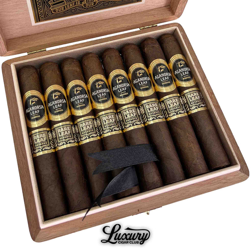 Close-up of Aganorsa Leaf Rare Leaf Reserve Maduro Robusto cigars with dark brown wrappers, black and gold bands, arranged in an open cedar box, Luxury Cigar Club.