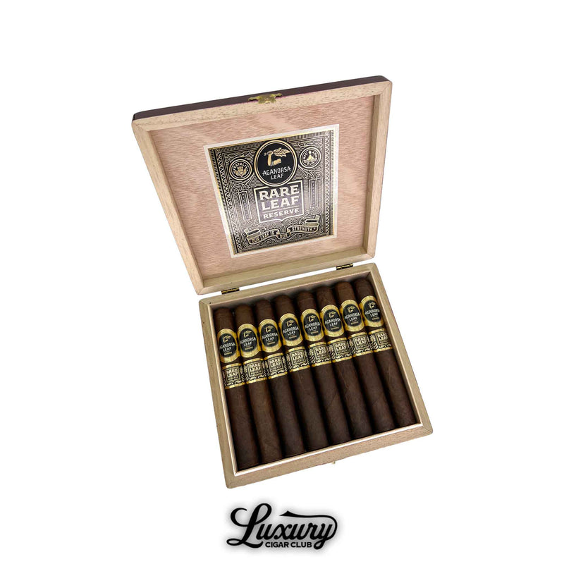 Open wooden box of Aganorsa Leaf Rare Leaf Reserve Maduro Toro cigars, displaying dark brown wrappers and elegant black-and-gold bands with the Aganorsa Leaf and Rare Leaf Reserve logos. Luxury Cigar Club branding below.