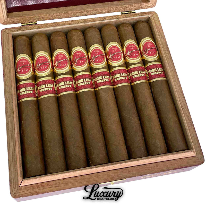 Close-up of Aganorsa Leaf Rare Leaf Reserve Toro cigars with red and gold bands inside an open wooden box at Luxury Cigar Club.