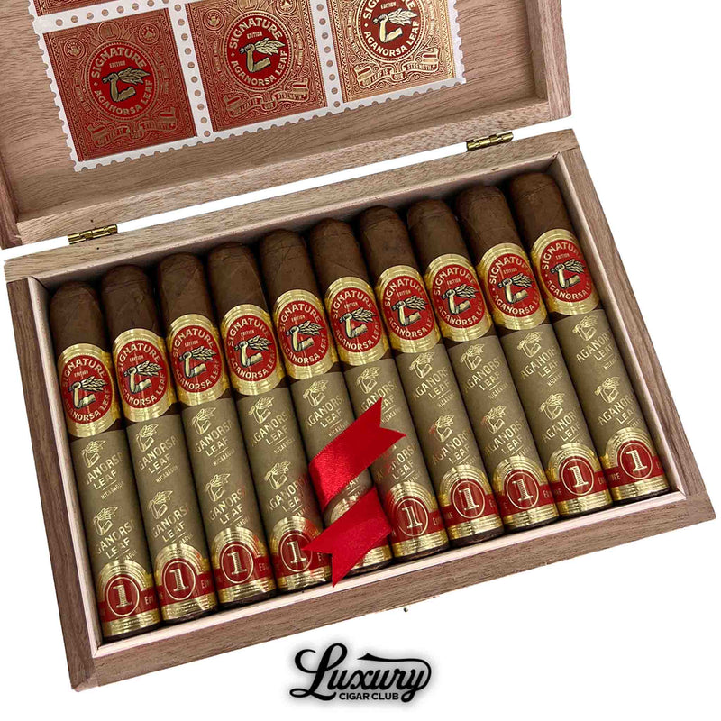 Close-up view of Aganorsa Leaf Signature Selection Robusto cigars in box with gold foil wrapping, red bands, and decorative stamp design, Luxury Cigar Club.