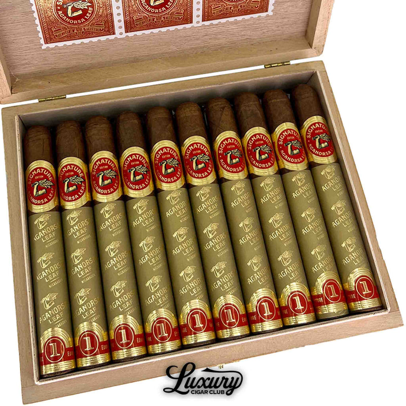 Close-up of Aganorsa Leaf Signature Selection Toro cigars inside a cedar box, showcasing gold foil wrapping and red “Signature Edition” bands with the Aganorsa Leaf logo. Luxury Cigar Club branding.