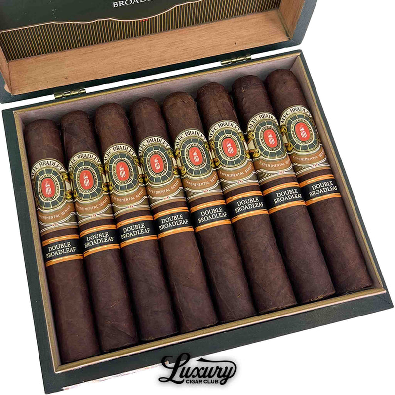Close-up of Alec Bradley Experimental Series Double Broadleaf Robusto cigars tightly packed inside a green cigar box showcasing dark broadleaf wrapper and intricate band artwork, Luxury Cigar Club branding at bottom.