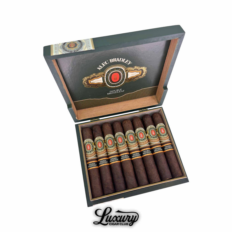 Open box of Alec Bradley Experimental Series Double Broadleaf Robusto cigars displayed neatly in rows with ornate black, gold, and red cigar bands inside a green velvet-lined wooden box on a white background, Luxury Cigar Club branding at bottom.