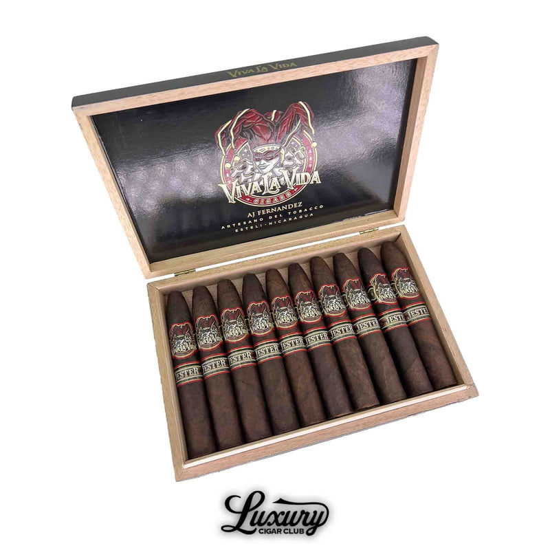 Open box of Artesano Del Tobacco Viva La Vida 5th Anniversary Jester Flat Round Belicoso cigars, handcrafted by AJ Fernandez in Estelí, Nicaragua, showcasing the jester-themed bands and neatly arranged dark-wrapped cigars in a wood-lined display.