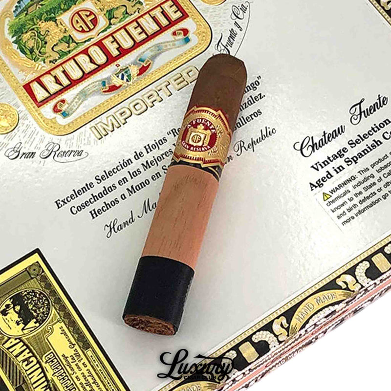 Close-up of Arturo Fuente Chateau Fuente Sun Grown cigar with cedar sleeve resting on its ornate box, featured by Luxury Cigar Club.