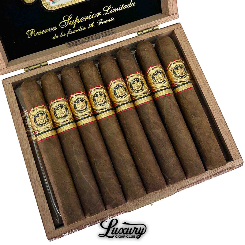 Close-up of a box of Arturo Fuente Don Carlos Doble Robusto cigars, showing 8 rich brown cigars with detailed black, gold, and red bands. The box interior reads “Reserva Superior Limitada de la familia A. Fuente,” with “Luxury Cigar Club” branding at the bottom.