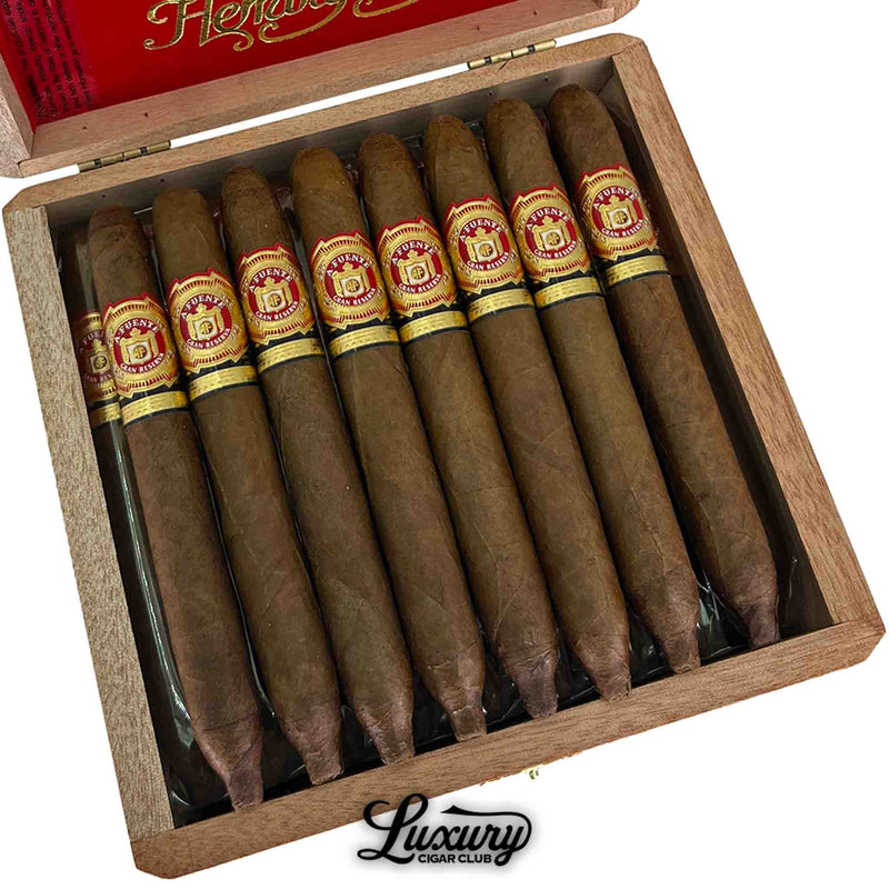 Close-up of Arturo Fuente Hemingway Signature cigars in an open wooden box, showcasing ten elegant, torpedo-shaped cigars with smooth brown wrappers and detailed red and gold bands, under a red lid with “Hemingway” script and the Luxury Cigar Club logo below.