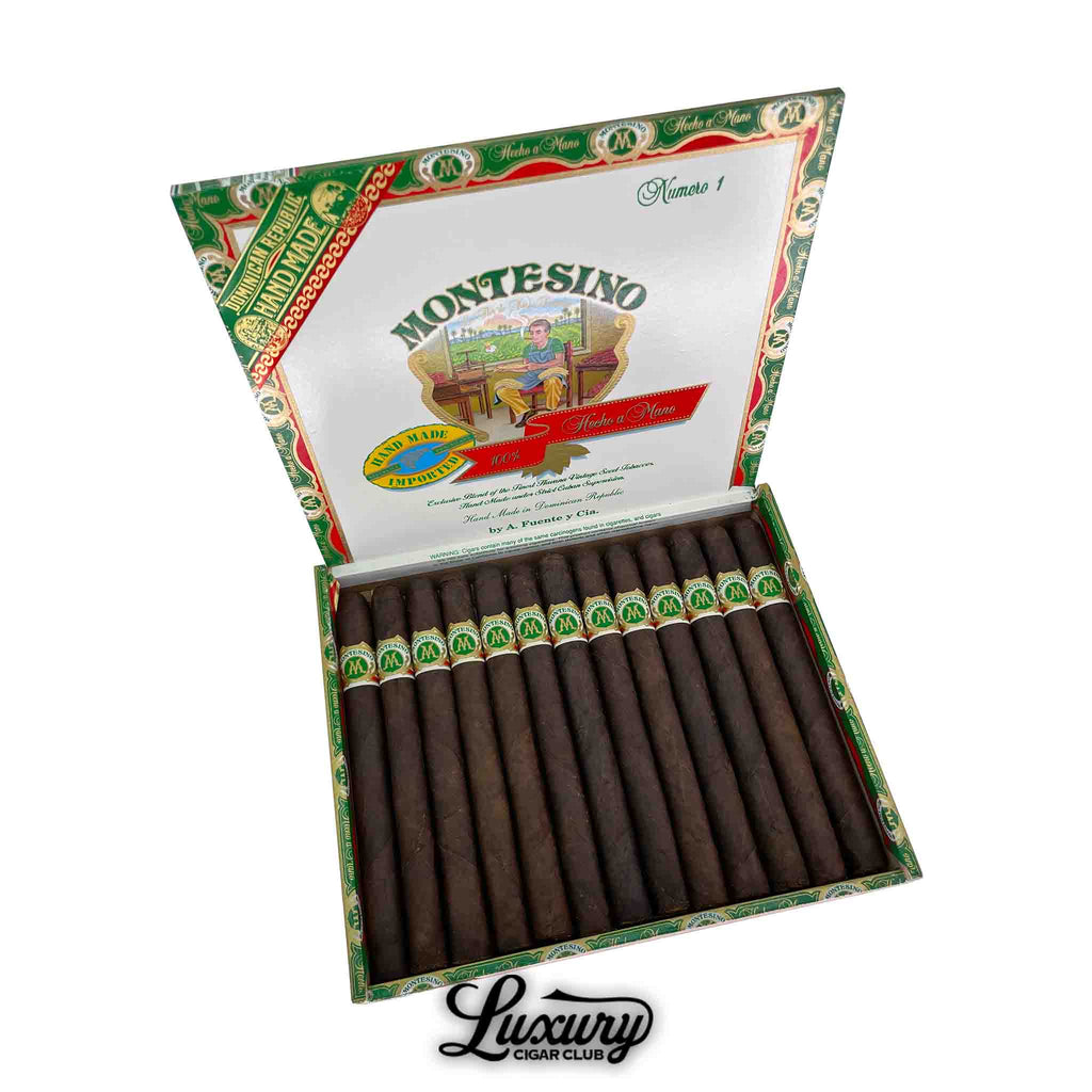 Open box of Montesino Maduro Numero 1 cigars by Arturo Fuente, displaying dark, well-aged cigars with green and gold bands, set against a decorative red, green, and white box interior labeled "Hecho a Mano" and "Luxury Cigar Club" branding below.