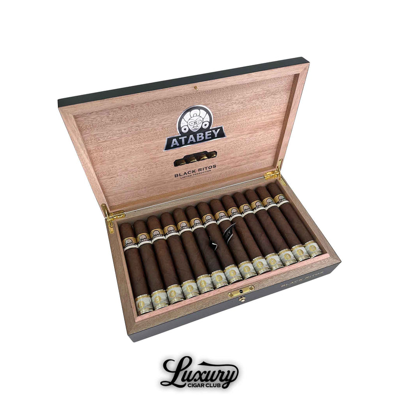 Open wooden cigar box displaying Atabey Black Ritos cigars, each with black, white, and gold bands, arranged in two neat rows under the branded lid.