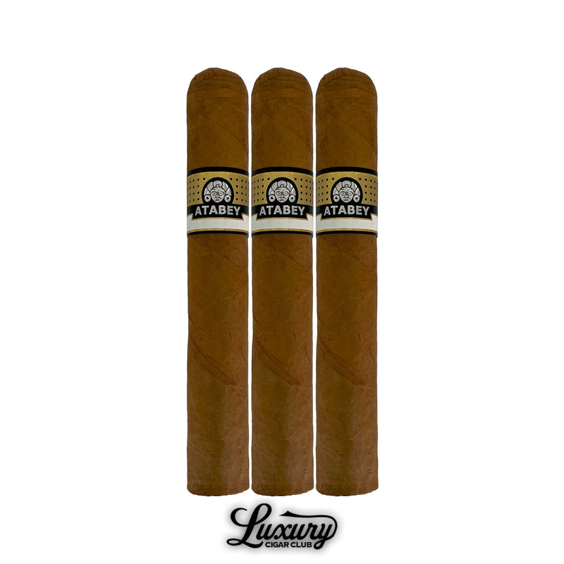 Trio of Atabey Delirios cigars showcasing Connecticut shade wrapper, traditional cylindrical shape, black and gold Atabey branding bands, golden foot details, standing above Luxury Cigar Club logo.