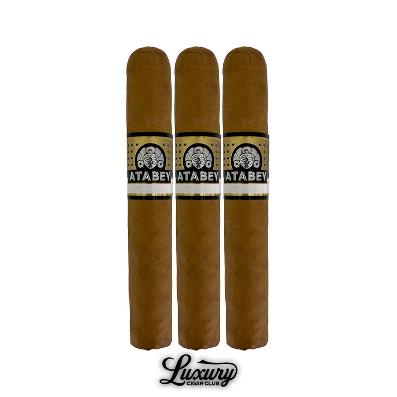 Three Atabey Hechizos cigars with pointed heads, light brown Connecticut shade wrapper, gold and black Atabey bands, golden foot bands, arranged upright in a row with Luxury Cigar Club logo beneath.