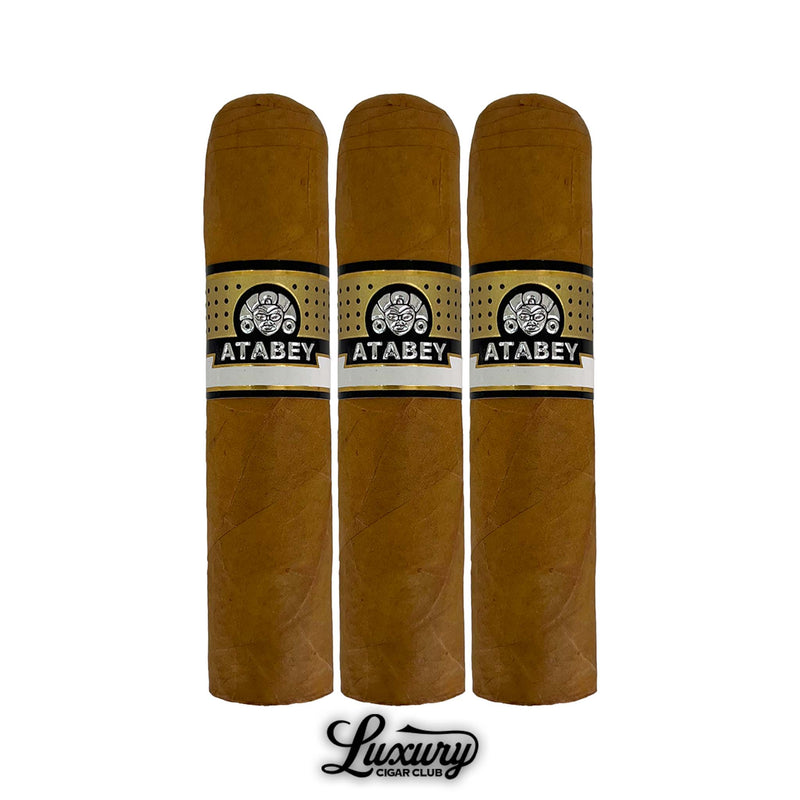 Trio of Atabey Idolos cigars featuring tan wrapper leaves, sleek construction, gold and black logo bands with golden foot details, aligned vertically above the Luxury Cigar Club logo.