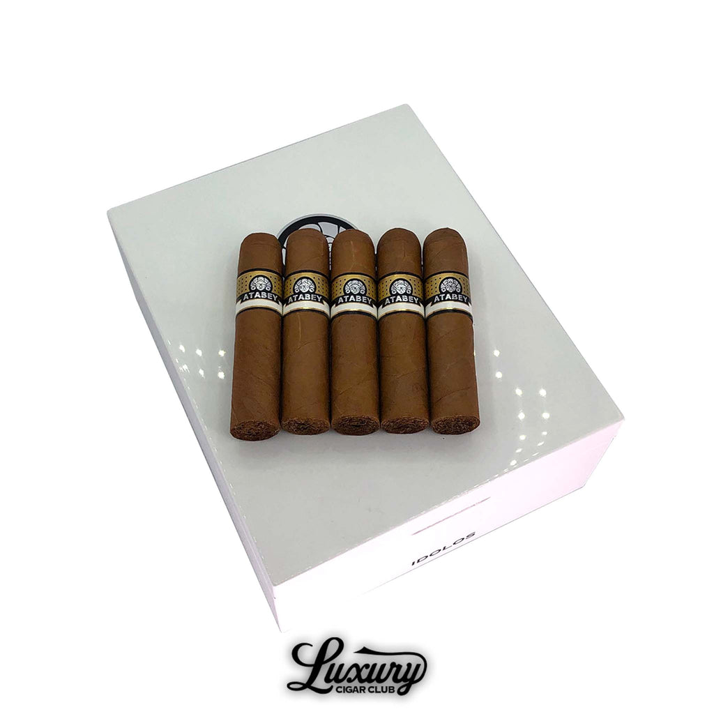 Five Atabey Idolos Cigars with golden Connecticut wrappers displayed on a glossy white humidor, highlighting luxury presentation and premium craftsmanship at Luxury Cigar Club