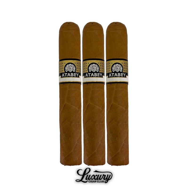 Three Atabey Sabios cigars with medium length, golden brown wrapper, black and gold Atabey bands, metallic gold foot rings, lined up with Luxury Cigar Club logo displayed below.