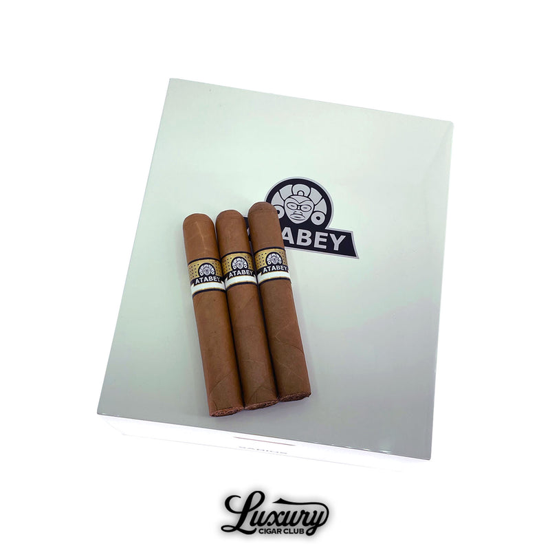 Three Atabey Sabios cigars resting on a pristine white Atabey humidor box, highlighting premium construction and signature banding, by Luxury Cigar Club.
