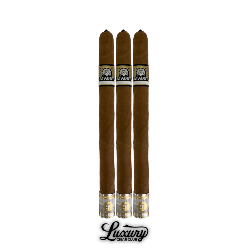 Three Atabey Spiritus cigars in long slim vitola, smooth golden brown wrapper, detailed Atabey bands in black and gold, golden foot embellishments, vertically arranged with Luxury Cigar Club branding below.
