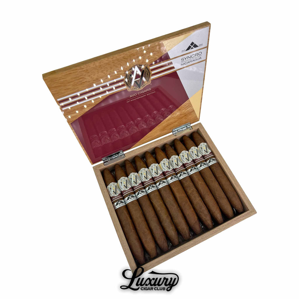 Open box of AVO Syncro Nicaragua 10th Anniversary Diadema cigars, featuring 10 uniquely tapered cigars with dual cream and maroon bands, arranged neatly in a wooden box with a glossy interior lid showcasing AVO branding and Syncro Nicaragua artwork; Luxury Cigar Club logo below.