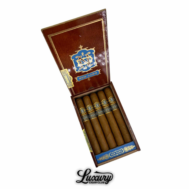 Open wooden box of Avowed New Dawn Toro cigars, showing five cigars with golden-brown wrappers and detailed blue and gold cigar bands, displayed at Luxury Cigar Club.