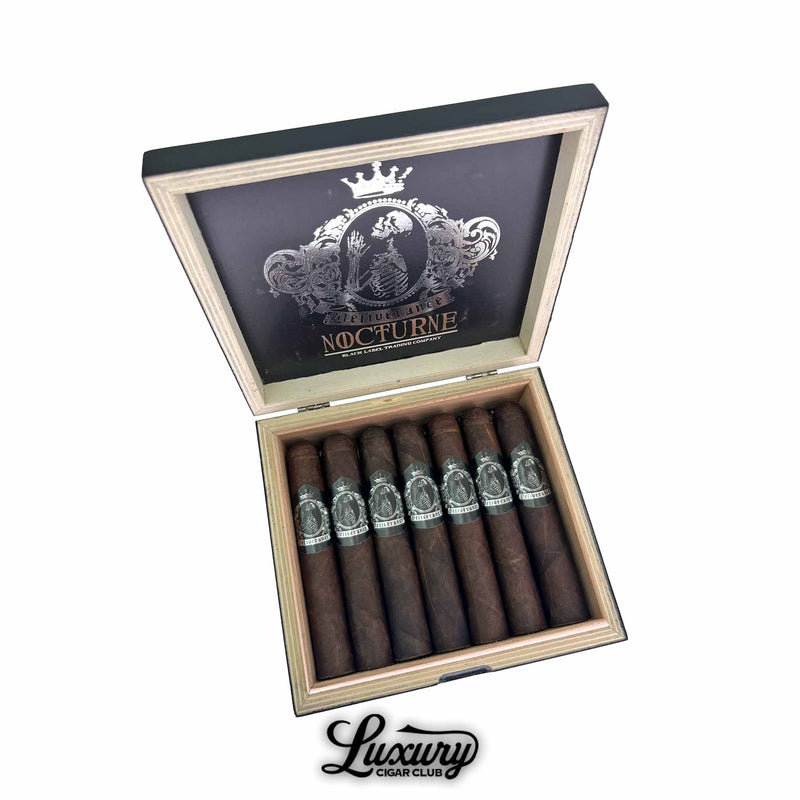 Open box of Black Label Trading Co. Deliverance Nocturne Robusto cigars displayed by Luxury Cigar Club with dark oily wrappers and silver skeletal crest bands arranged in two rows.
