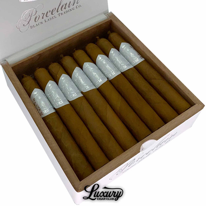 Close-up of Black Label Trading Co. Deliverance Porcelain Corona Gordo cigars arranged in a white box, highlighting their light Connecticut wrappers and elegant silver foil bands, presented by Luxury Cigar Club.