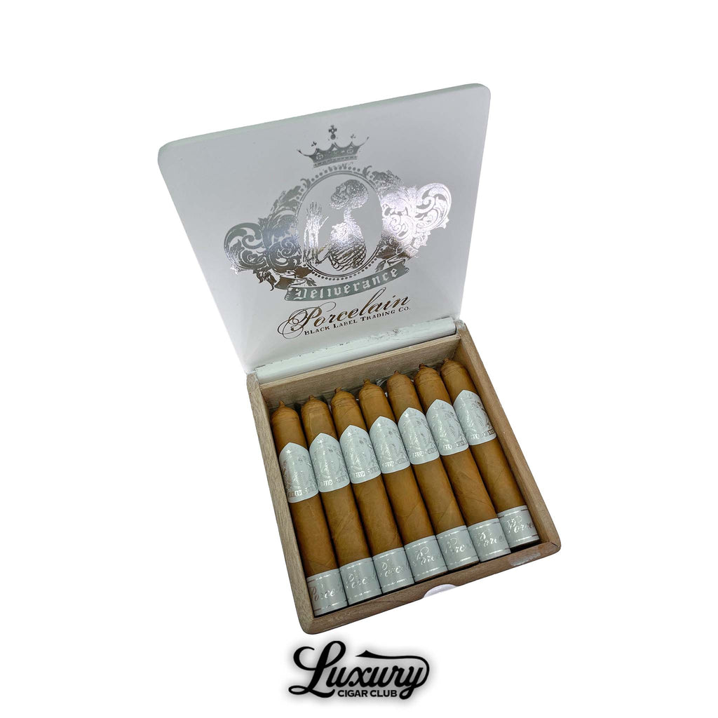 Black Label Trading Co. Deliverance Porcelain Robusto cigars neatly arranged in a white box with silver embossed crest design on the lid, showcasing light Connecticut wrappers, presented by Luxury Cigar Club.