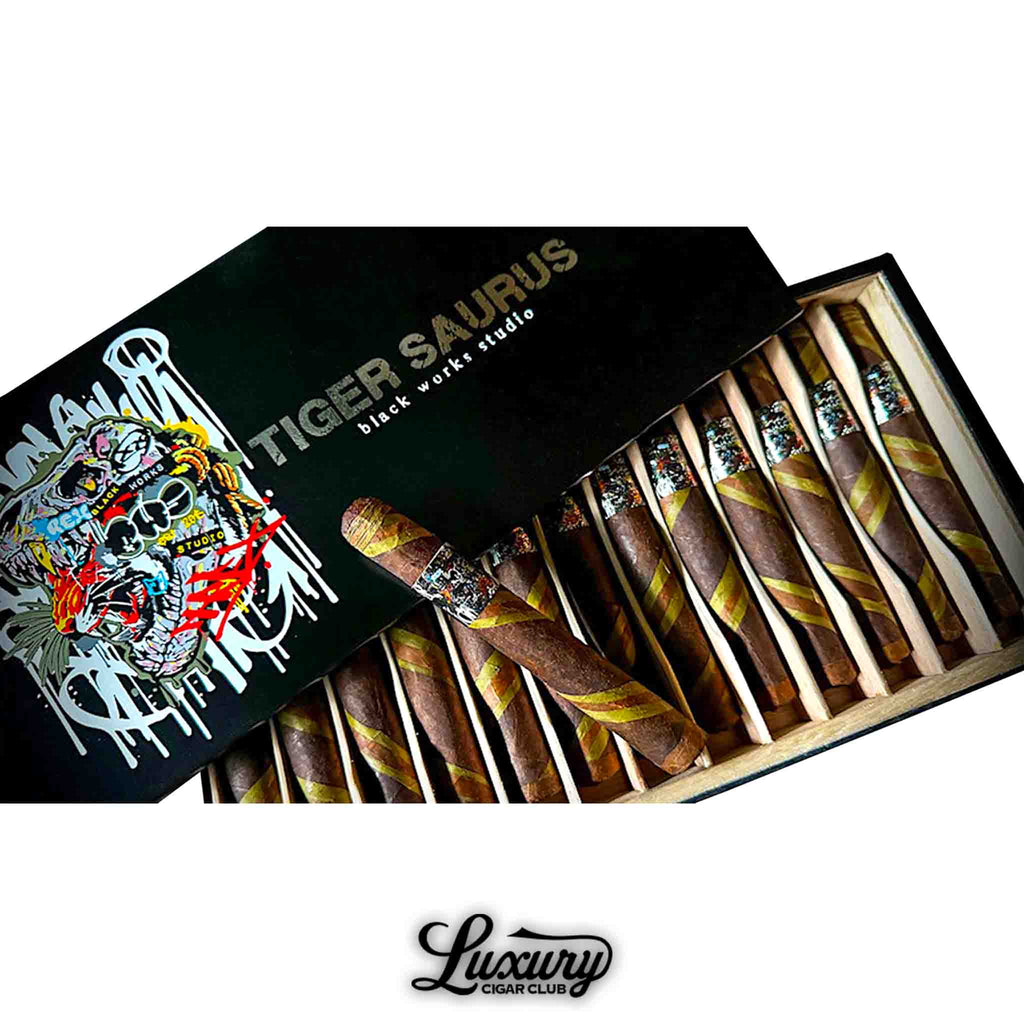 Open black and gold box of Black Works Studio Tigersaurus Corona Gorda cigars with bold band artwork and barber pole wrappers, presented by Luxury Cigar Club.