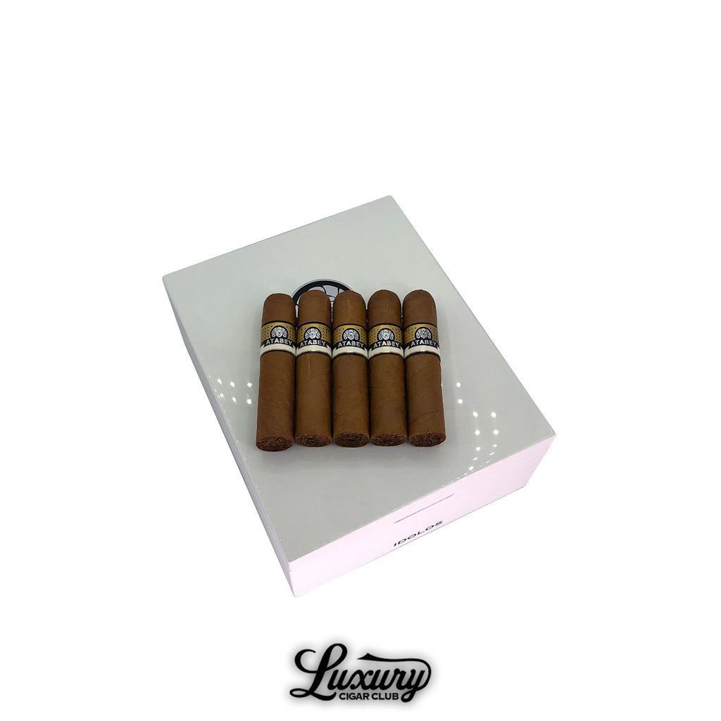 Five Atabey Idolos Cigars with golden Connecticut wrappers displayed on a glossy white humidor, highlighting luxury presentation and premium craftsmanship at Luxury Cigar Club