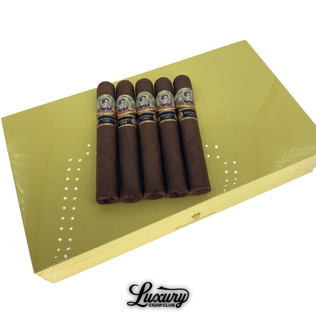 Byron 20th Century Londinenses cigars displayed on top of a glossy yellow humidor box, featuring five dark-wrapped cigars with blue, gold, and red Reserva 4 Años bands, available at Luxury Cigar Club.