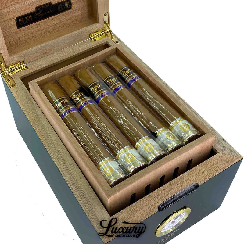 Close-up view of Byron 21st Century Elegantes cigars inside a luxury humidor, showing detailed gold and blue cigar bands, cellophane protection, and rich wood grain finish with Luxury Cigar Club branding.