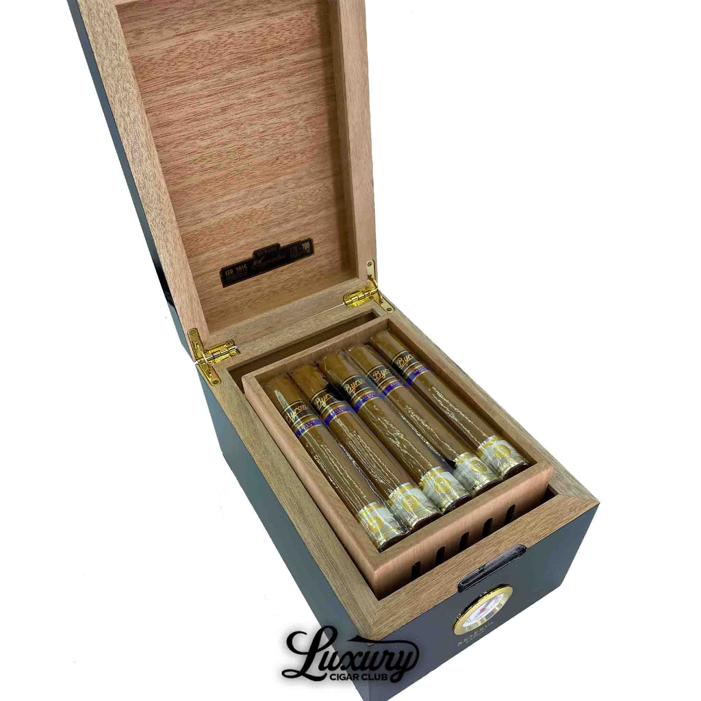 Open black and wood humidor box of Byron 21st Century Elegantes cigars, each wrapped in cellophane with gold and blue bands, displayed at an angle with Luxury Cigar Club logo at the bottom.