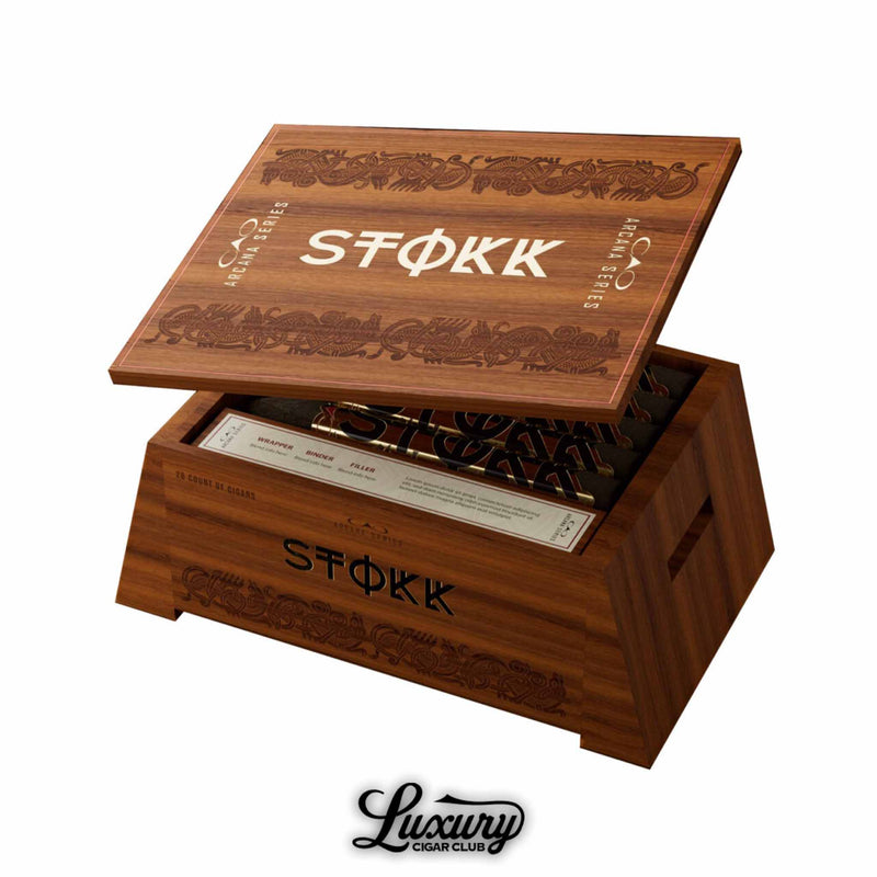 Open wooden cigar box of CAO Arcana Series Stokk Limited Edition cigars, featuring bold engraved lettering and ornate designs on the lid and sides, displayed at an angle with visible cigars inside; Luxury Cigar Club logo beneath.