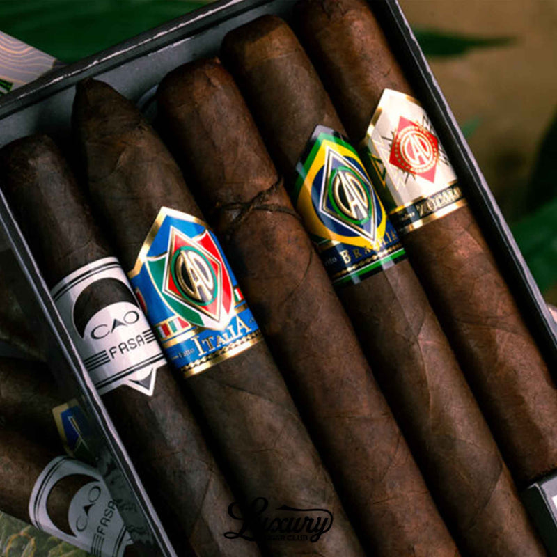 Close-up detail of CAO Outpost Volume Two sampler showing dark wrapper cigars with Italia, Brazilia, Zócalo and Fuma Em Corda bands inside the sampler tray, shot for Luxury Cigar Club.