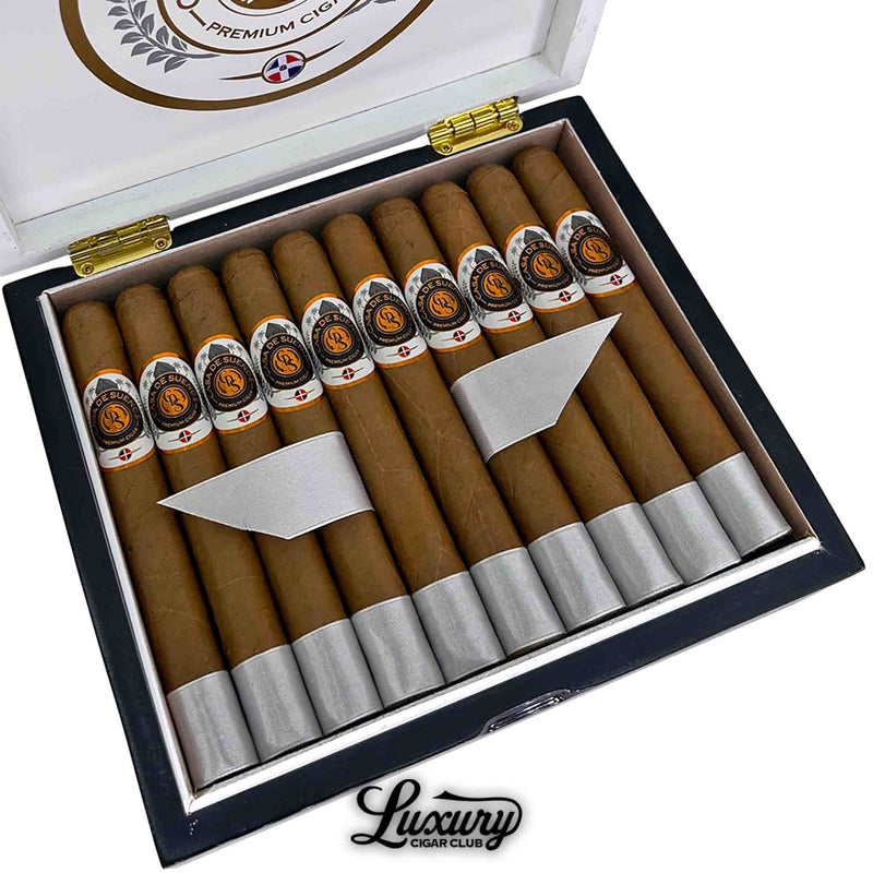 Close-up of Casa de Sueños Angelito Corona cigars arranged neatly in a white and black box. Each cigar features a detailed Casa de Sueños band with gold accents and a silver foot wrap. Luxury Cigar Club logo beneath.