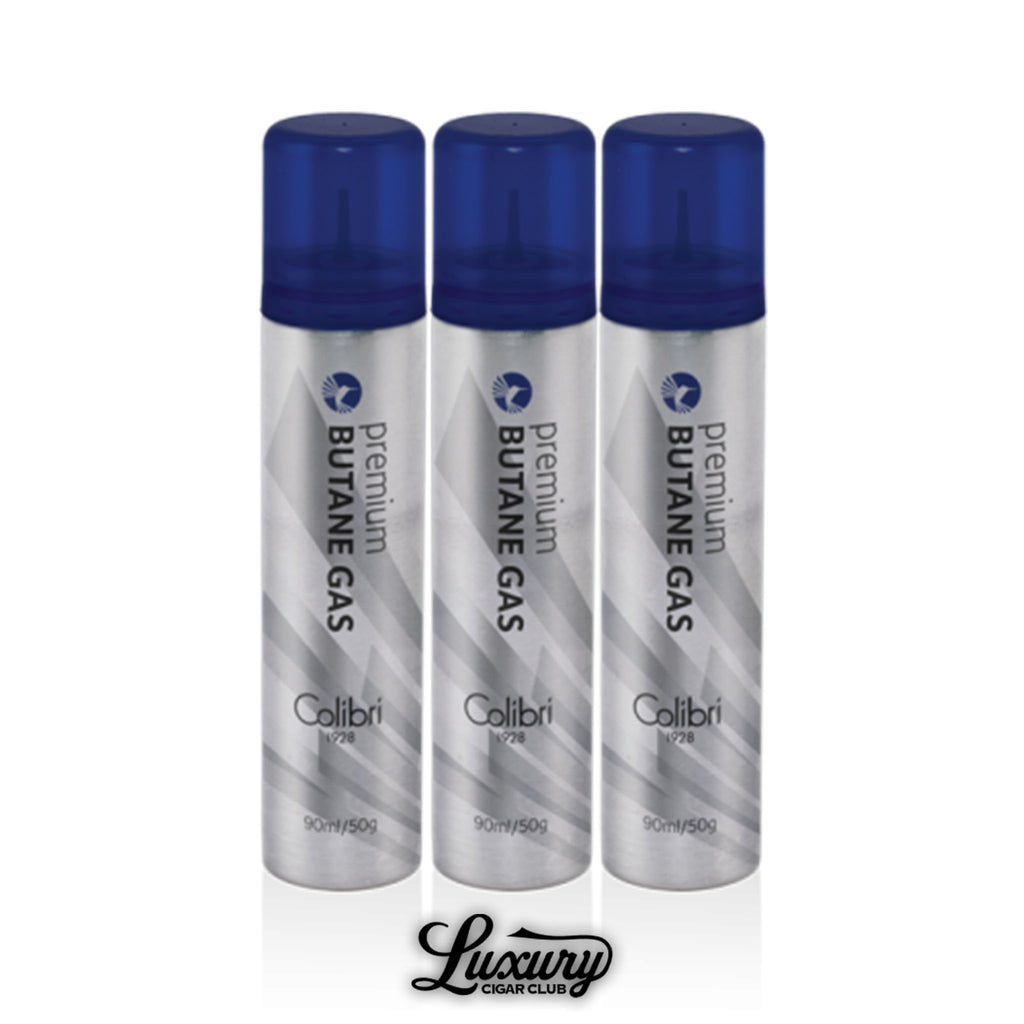 Colibri Premium Butane Gas 12-Pack for cigar lighters, featuring ultra-refined 99.9994% pure butane in silver cans with blue caps, displayed in a grouped set. Luxury Cigar Club logo shown at bottom.
