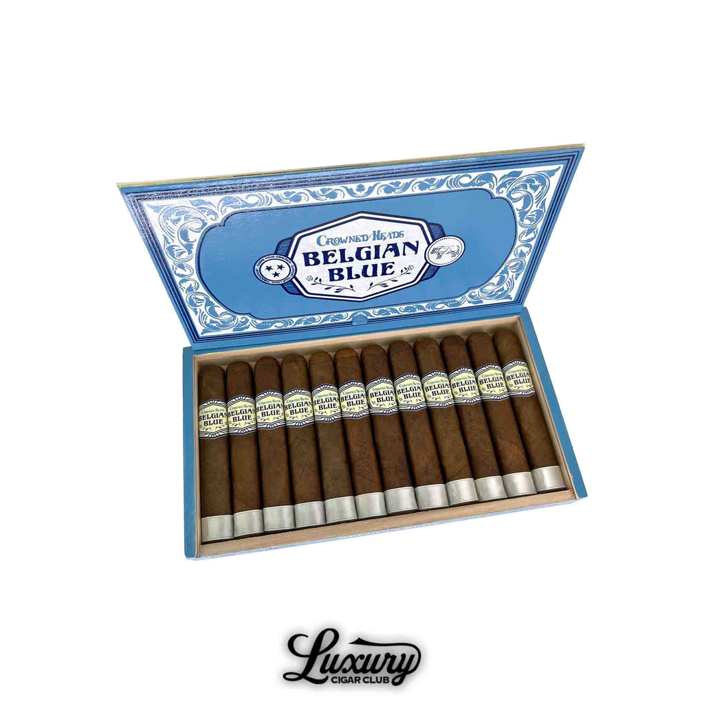 Open box of Crowned Heads Belgian Blue Limited Edition 2025 Double Robusto BP cigars, arranged in a single row inside a light-blue, decorative box. The cigars feature a medium-brown wrapper, each with a cream and blue Belgian Blue band and silver foot band. The inner lid shows the Belgian Blue logo with ornate border artwork. Luxury Cigar Club watermark below.